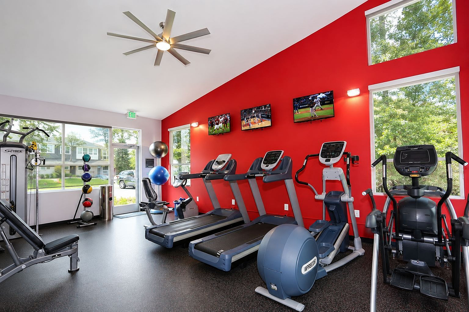 Vibrant fitness center showcasing modern treadmills, elliptical machines, and strength training equipment against a bold red wall with mounted TVs.