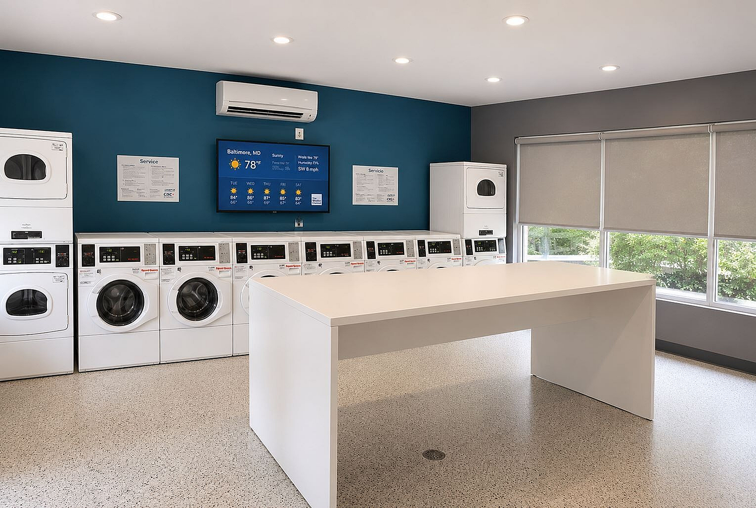 Modern laundry room with multiple washing machines and dryers, featuring a sleek white folding table and a digital display on a vibrant blue wall.