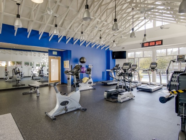 Fitness center with high ceiling with ellipticals, treadmills, stationary bikes, and free weights.