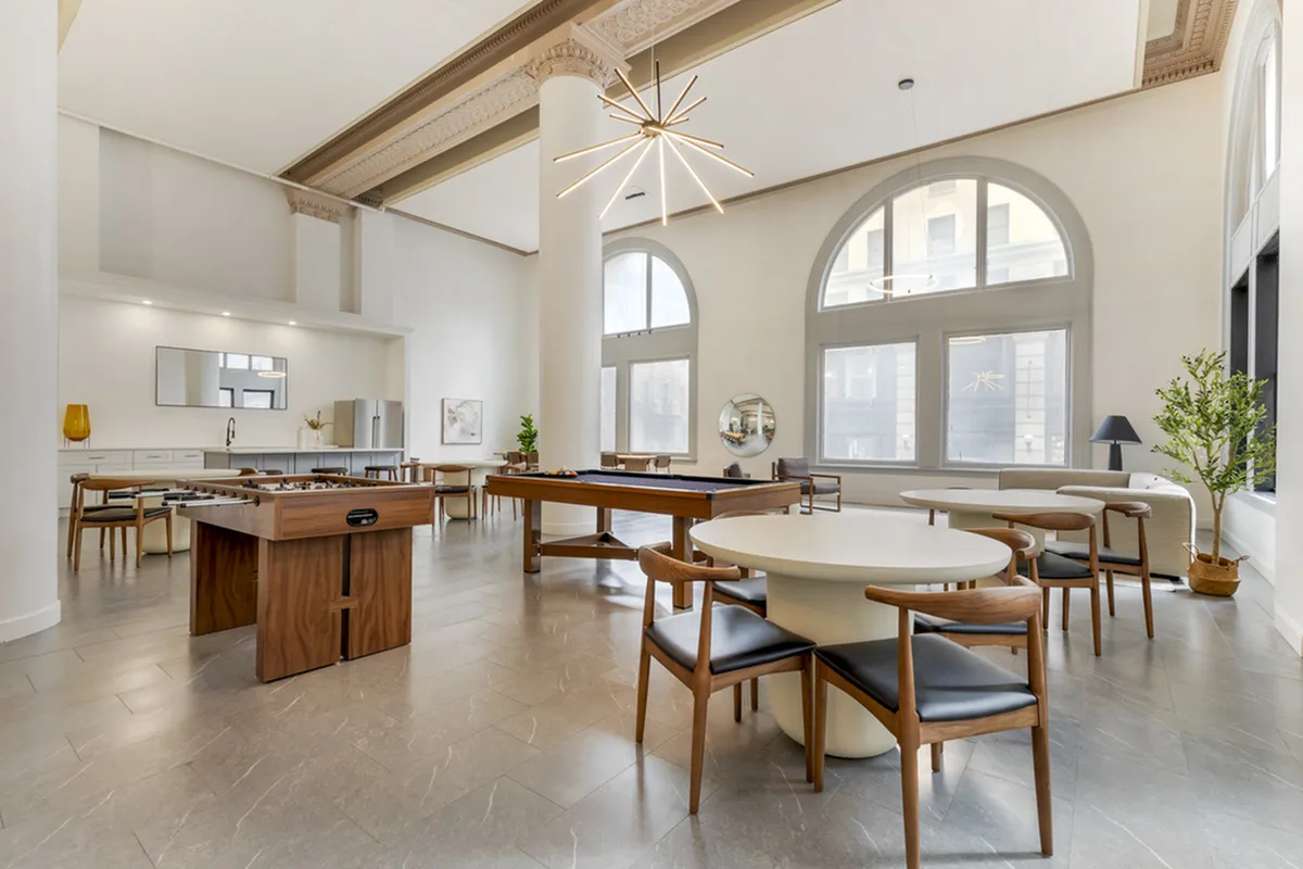 Spacious communal lounge with elegant decor featuring high ceilings, large windows, and a variety of modern furniture including a game table and sleek dining set