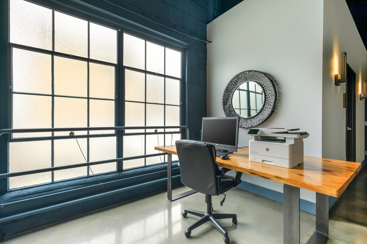 Bright community business center with large industrial-style windows, sleek furnishings, and wall art mirror.