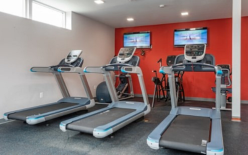 Modern fitness room with state-of-the-art treadmills and vibrant red accent wall, perfect for an energizing workout.