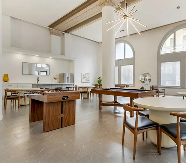 Spacious apartment amenity area with modern furniture, high ceilings, and large windows.