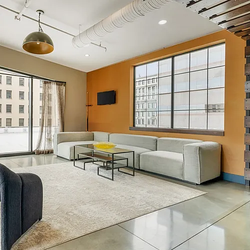 Bright modern apartment lounge with large windows, stylish furniture, and city view.