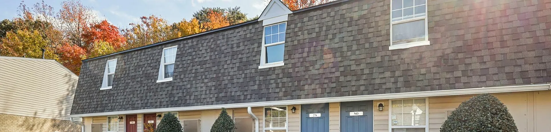 Charming townhome exterior with blue and red doors, surrounded by lush greenery and autumn trees.