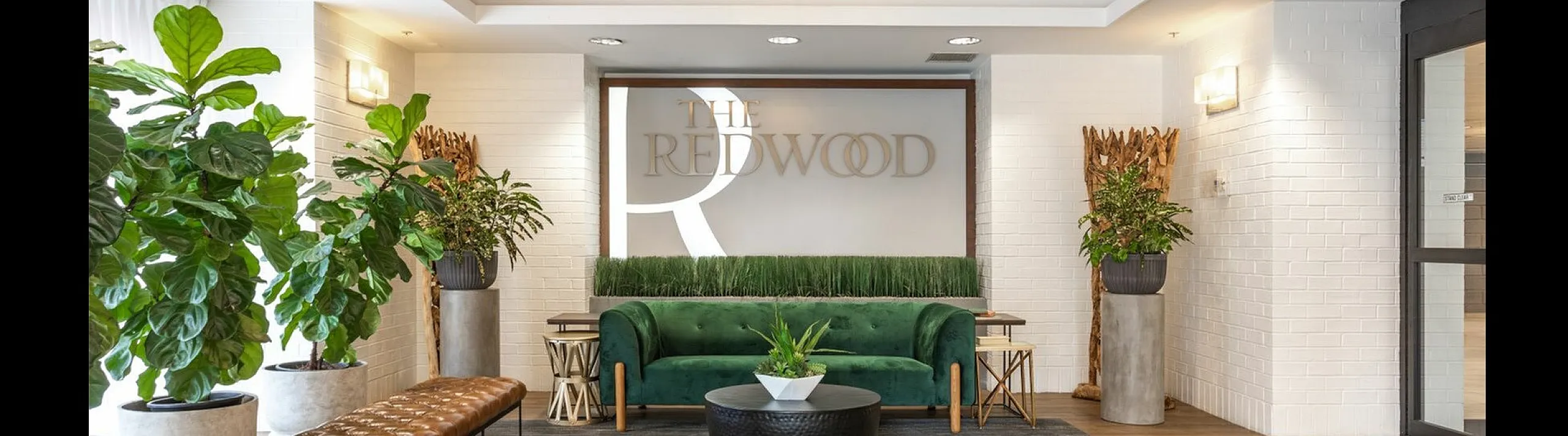 Stylish lobby with a green velvet sofa, leather bench, and lush plants at The Redwood.