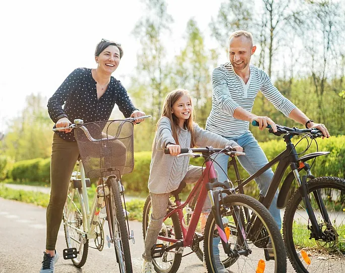 Happy family cycling together in a sunny park, enjoying outdoor activities.
