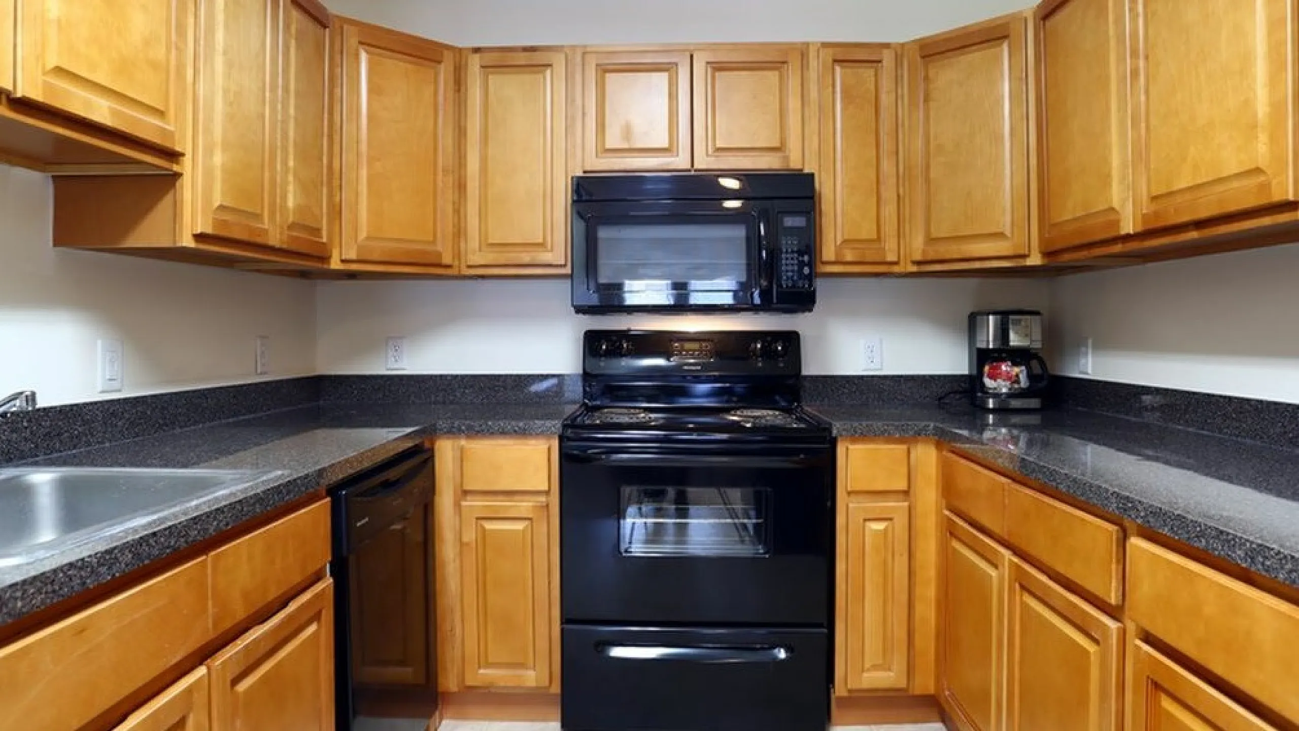 Spacious U-shaped kitchen with wooden cabinetry, sleek black appliances, and modern countertops.