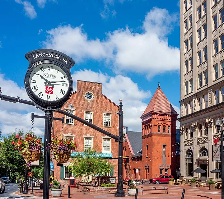 Charming Lancaster streetscape featuring a classic clock, historic brick buildings, and vibrant hanging flower baskets under a beautiful blue sky.