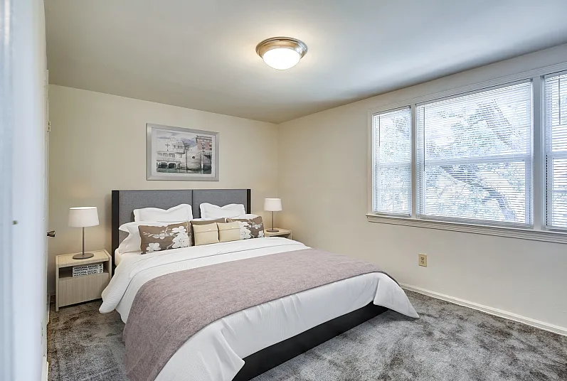 Bright and inviting bedroom with a plush bed, elegant decor, and natural light streaming through large windows.