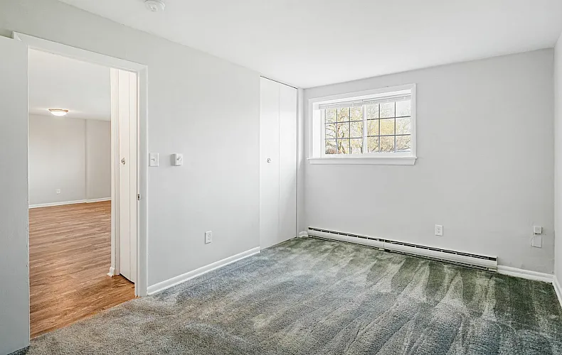 Bright and inviting room with plush carpet and large window offering natural light, perfect for creating a cozy living space.