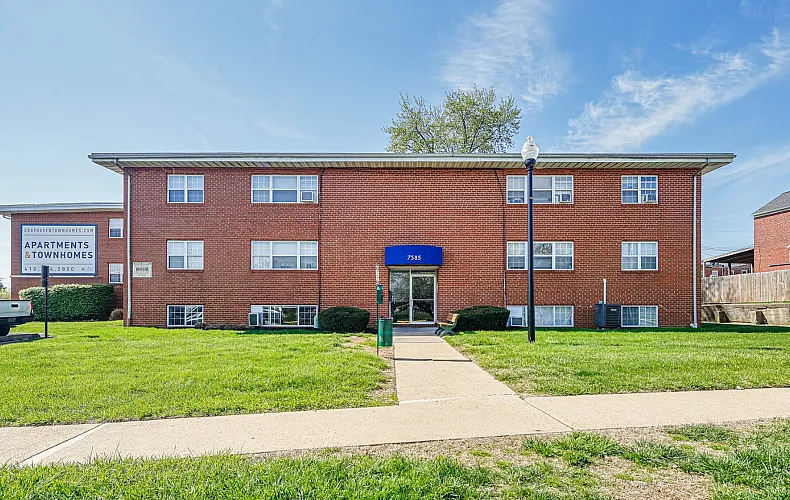 Charming brick apartment building surrounded by lush greenery under a bright blue sky.