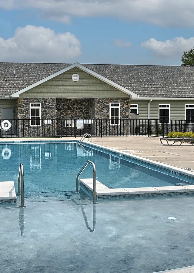 Inviting outdoor swimming pool with modern architecture, surrounded by lush greenery and a clear blue sky backdrop.