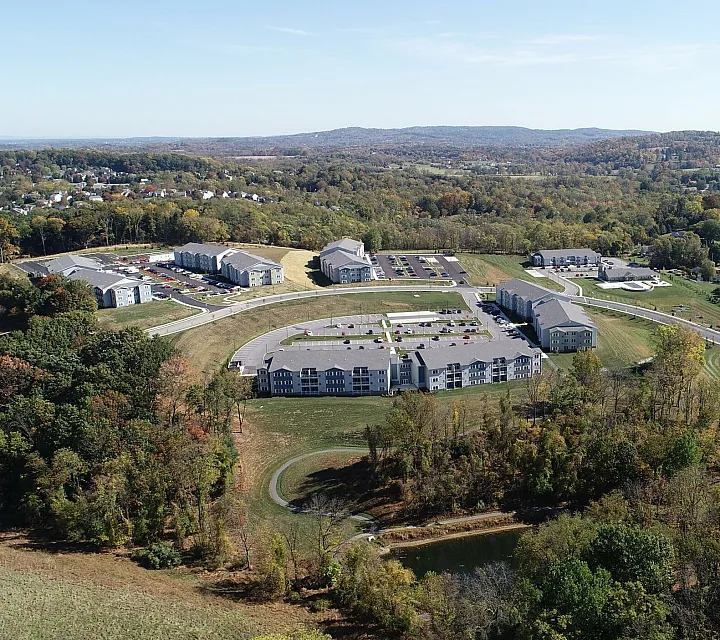 Breathtaking aerial view of a modern apartment complex nestled in lush, expansive greenery, showcasing serene living in a picturesque landscape.