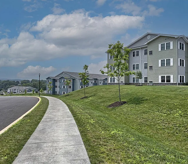 Charming apartment complex with modern architecture, lush green surroundings, and a scenic view under a vibrant blue sky.