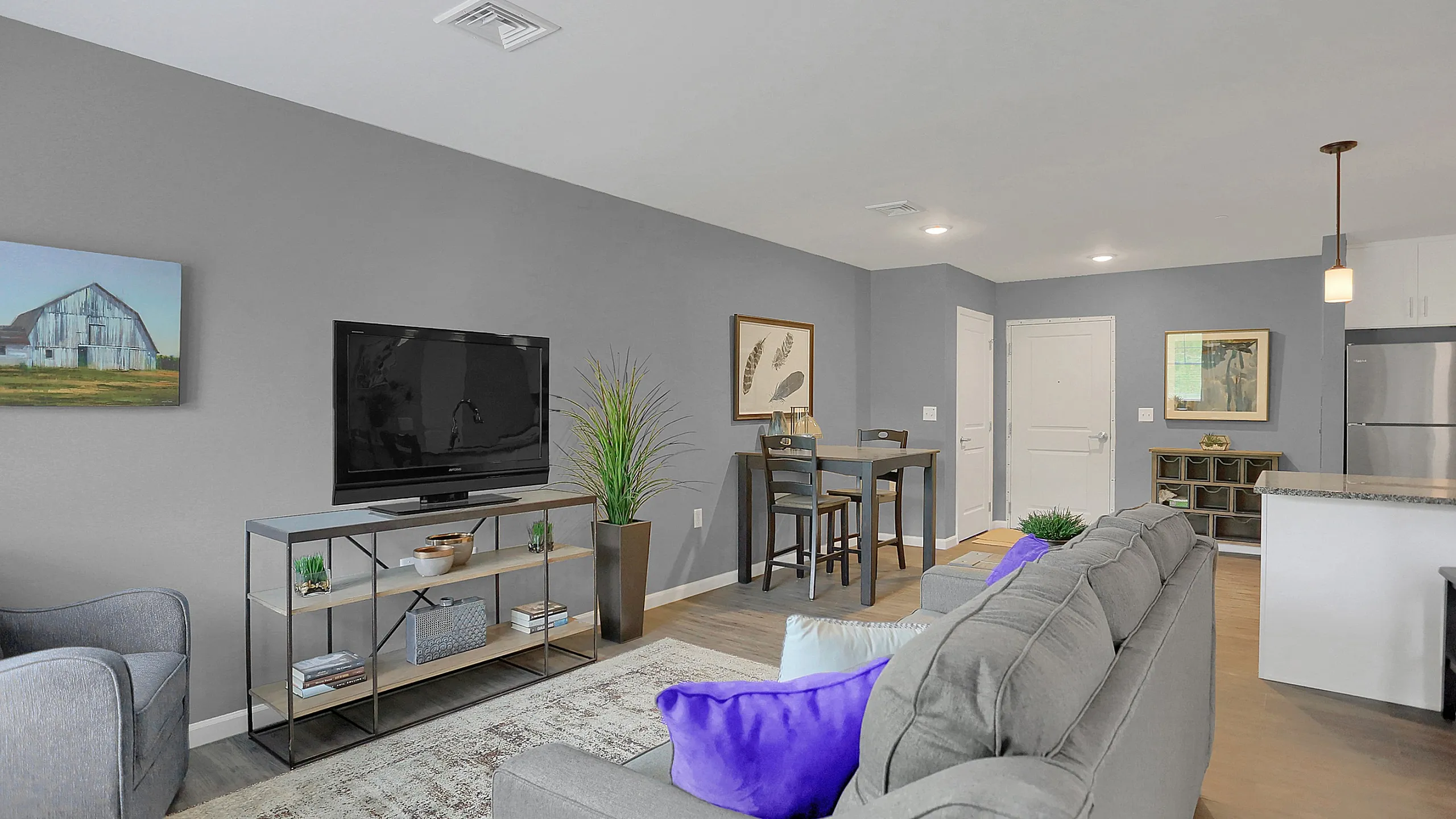 Modern living room with stylish gray walls, plush seating, vibrant purple cushions, and a chic entertainment center. Open-concept design adjacent to a cozy dining area and sleek kitchen.