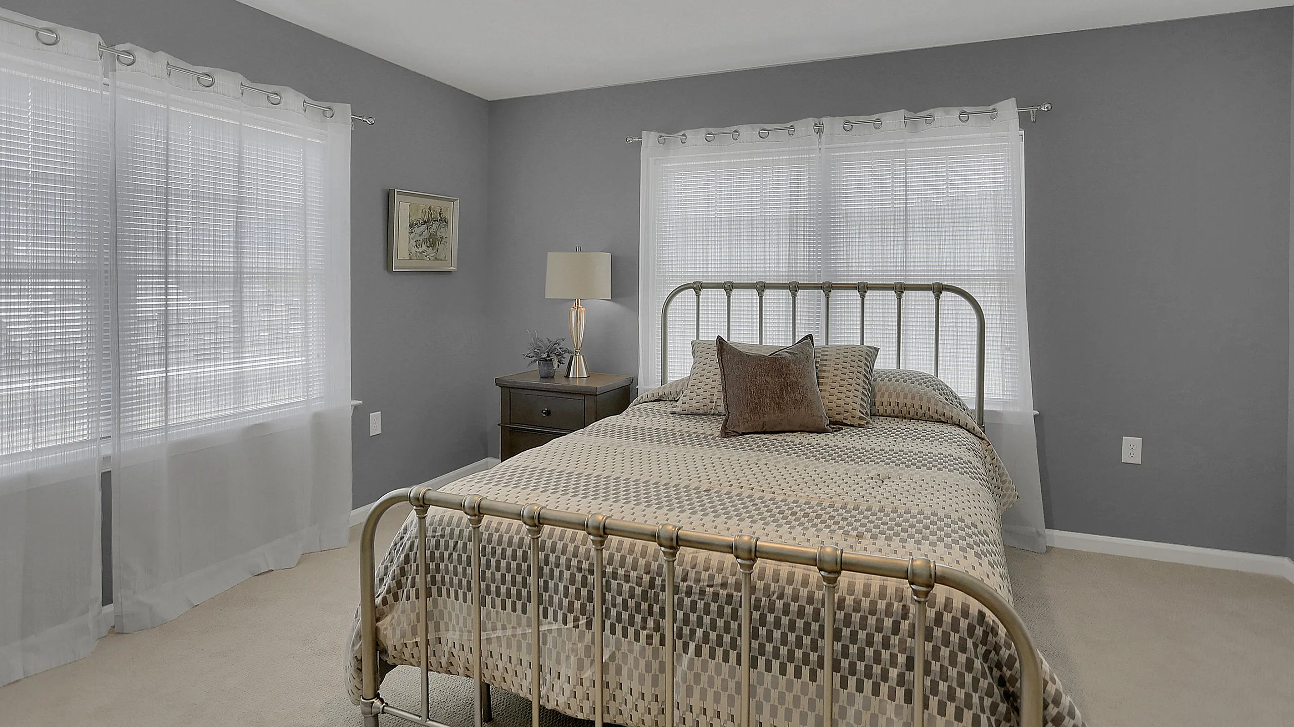 Inviting bedroom with chic decor, featuring a metal bed frame against a soothing gray wall and large sunlit windows.