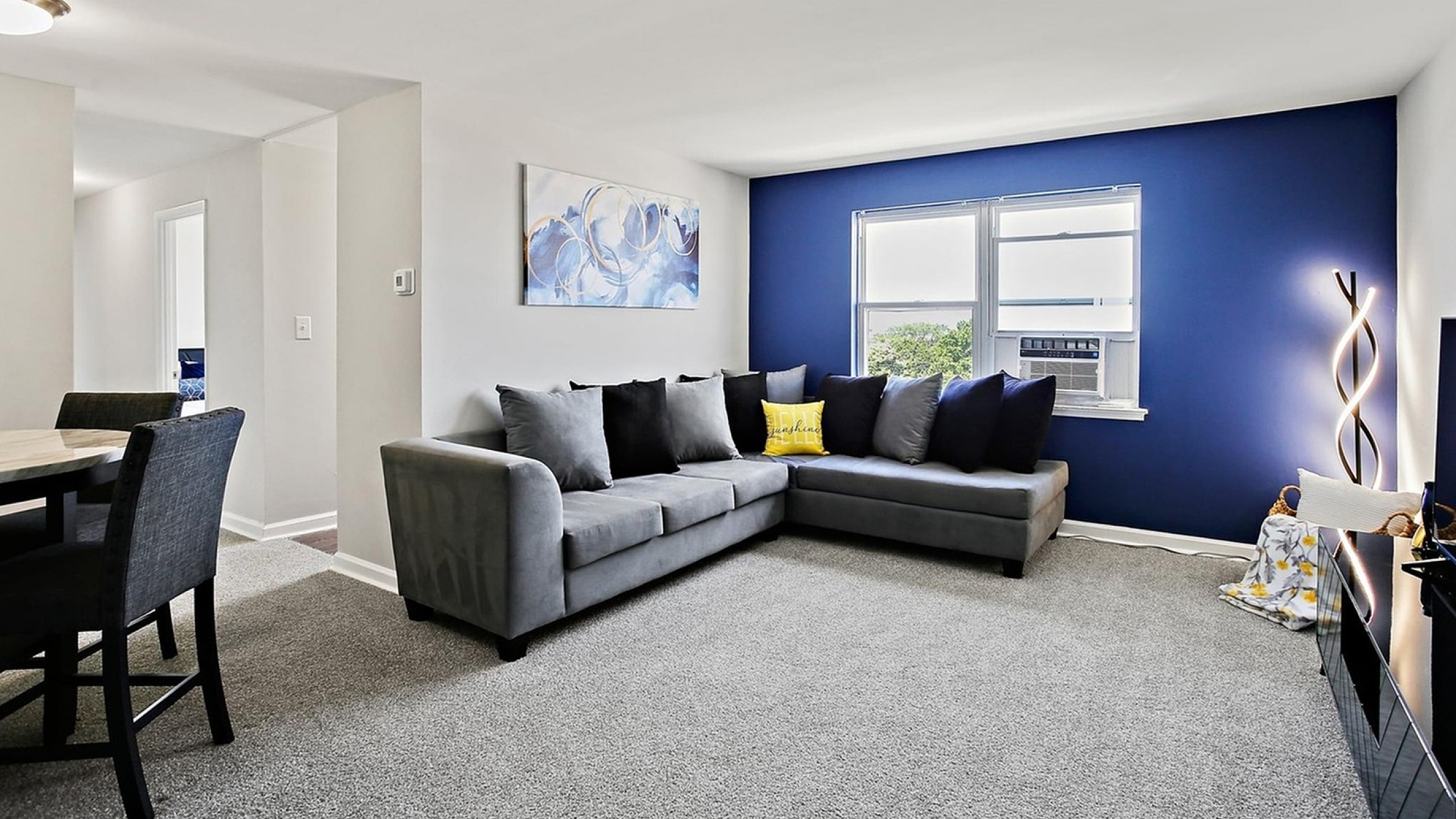 Modern living room with a stylish gray sectional sofa, vibrant blue accent wall, and elegant lighting, offering a cozy and inviting atmosphere.