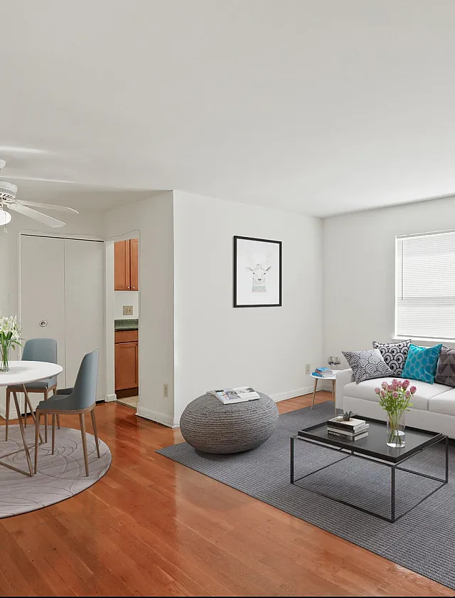 Bright and inviting living room with modern decor, featuring a cozy white sofa, vibrant throw pillows, and a sleek coffee table. Adjacent is a stylish dining area with a round table and contemporary chairs on warm hardwood floors.