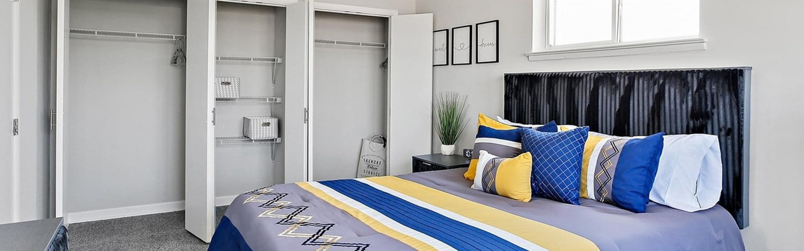 Inviting bedroom with modern decor, featuring a plush bed with colorful pillows, ample closet space, and stylish lighting.