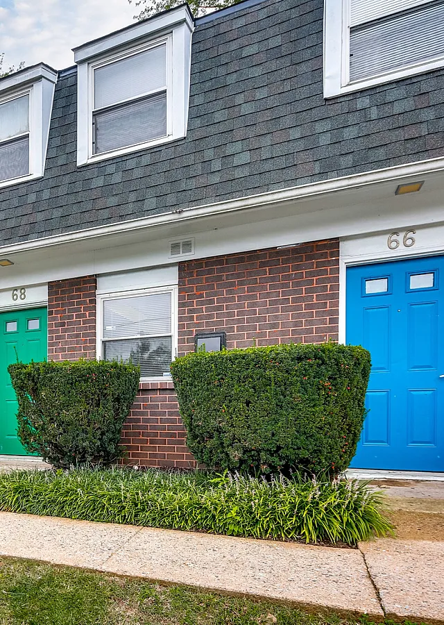 Charming townhouse exterior featuring colorful doorways, manicured shrubs, and a neatly paved walkway under a bright sky.