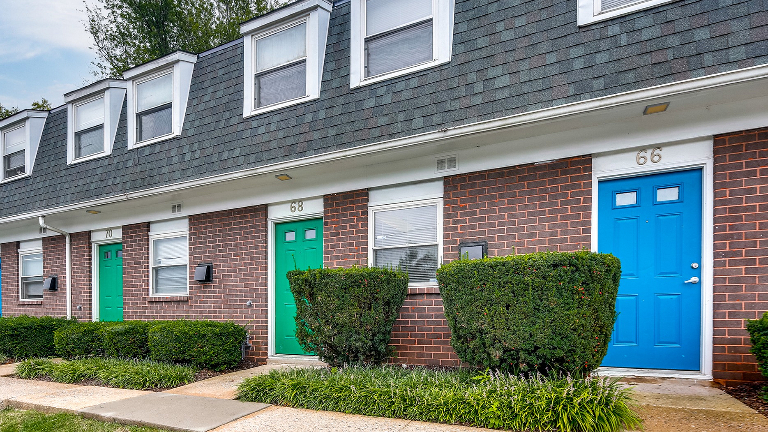 Charming townhouse exterior with colorful doors and manicured hedges, offering a welcoming and vibrant street view.