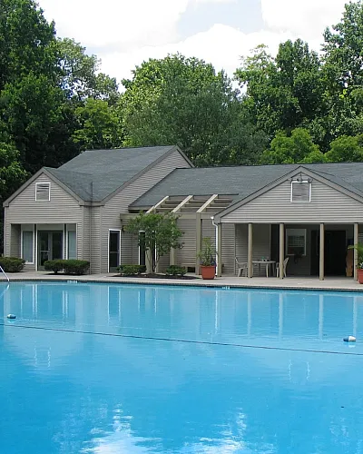 Inviting residential pool with a serene contemporary clubhouse surrounded by lush green trees, offering a perfect retreat for relaxation and leisure.