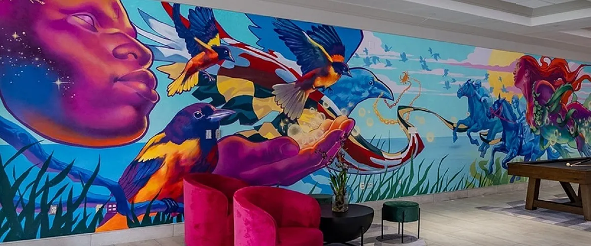 Vibrant contemporary lobby featuring stunning mural art with colorful birds and horses, complemented by plush pink seating and a stylish tile floor.