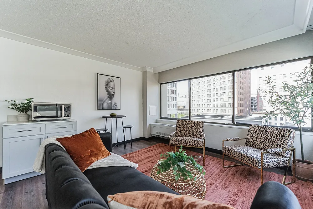 Chic urban living room with panoramic city views, featuring elegant cheetah-print chairs, a plush black sofa, and vibrant decor accents.
