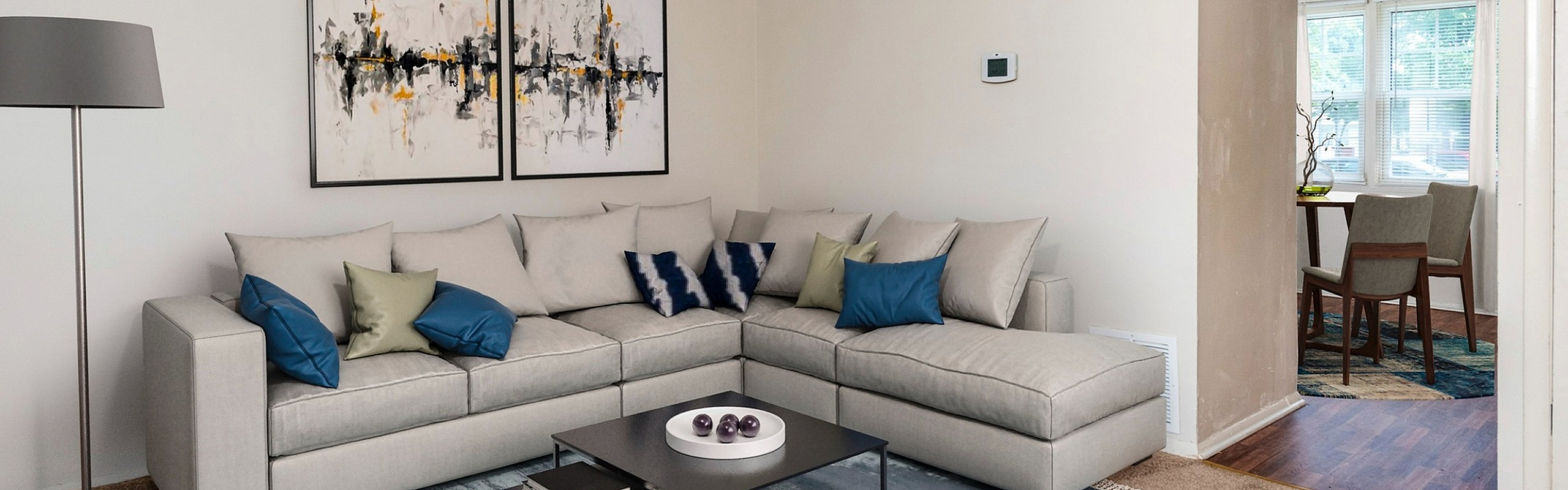 Inviting living room with plush sectional sofa, modern artwork, and a cozy dining area with natural light through large windows.