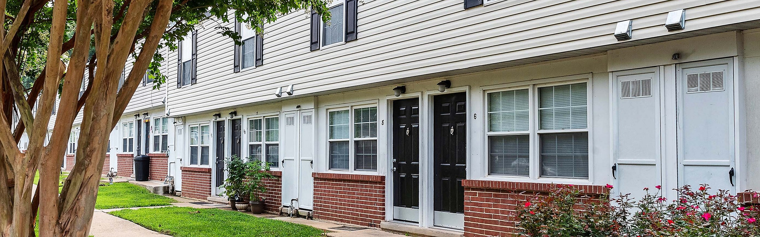 Charming townhomes with elegant brick exteriors, framed by lush greenery and a welcoming sidewalk.