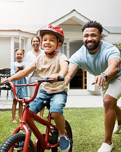 Charming backyard scene with a joyful family, highlighting a child learning to ride a bike under the warm sun, showcasing an inviting family-friendly home atmosphere.