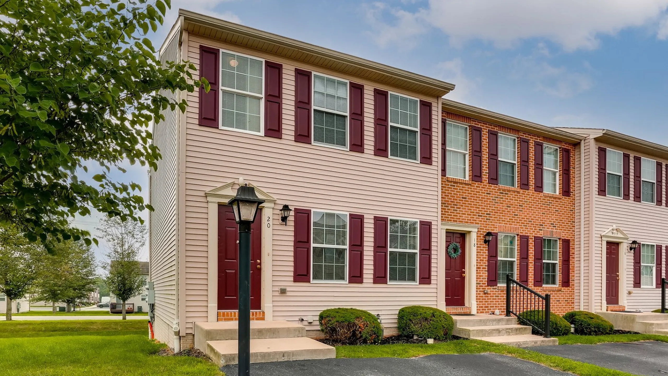 Charming end-unit townhouse with brick accents, vibrant shutters, and lush green surroundings.