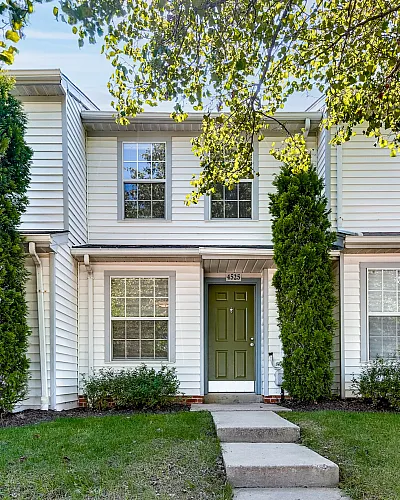 Charming townhouse exterior with classic white siding, manicured lawn, and vibrant green front door, nestled in a serene neighborhood.