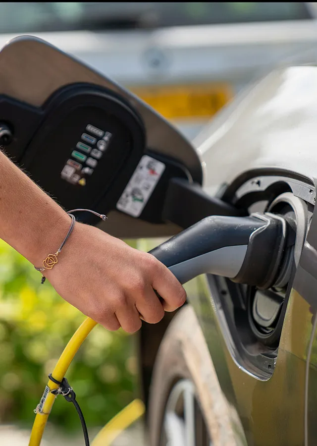 Close-up of a person charging an electric vehicle with a yellow cord, showcasing sustainable and modern transportation.