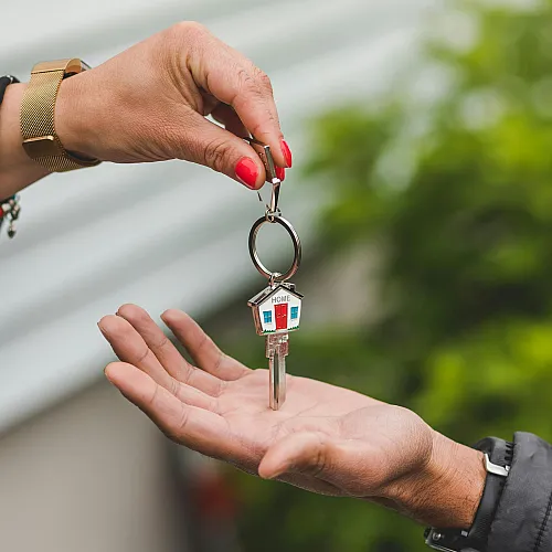 A symbolic handover of a house key with a charming home-shaped keychain, set against a lush green background.