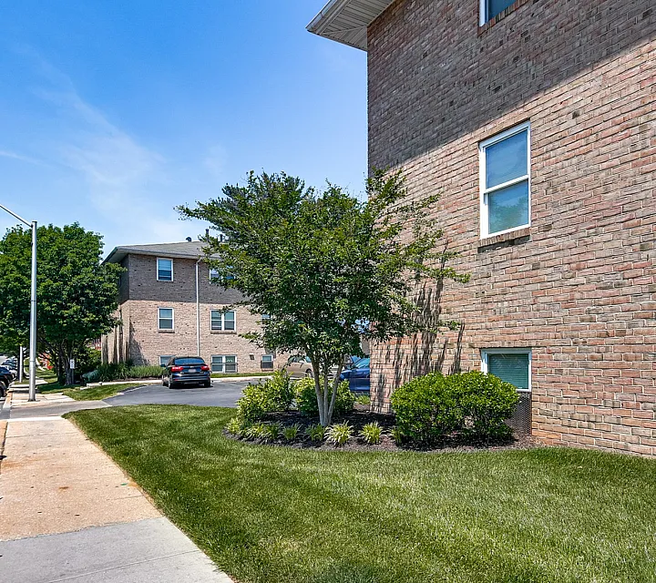 Charming brick exterior of Sequoia Manor Apartments with lush landscaping, serene environment, and available parking garages.