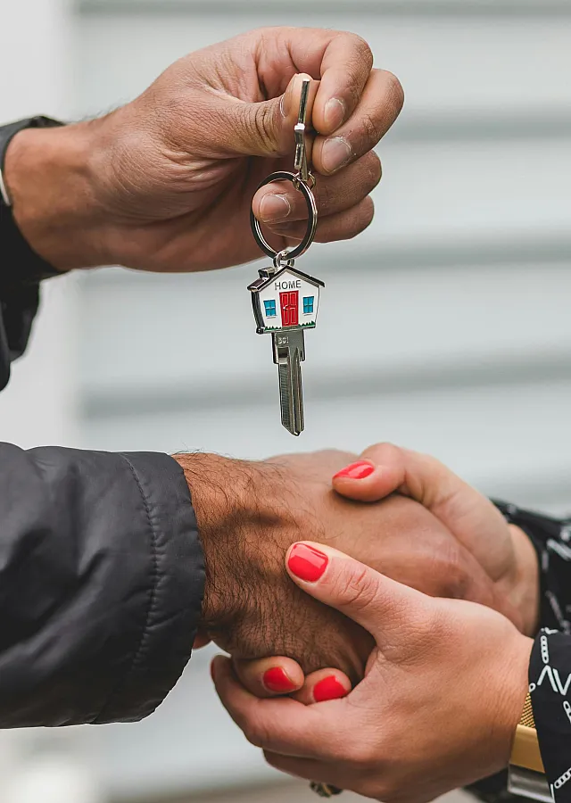 Close-up of a joyful moment, shaking hands with a new homeowner while holding a key with a house-shaped keychain, symbolizing a fresh beginning.
