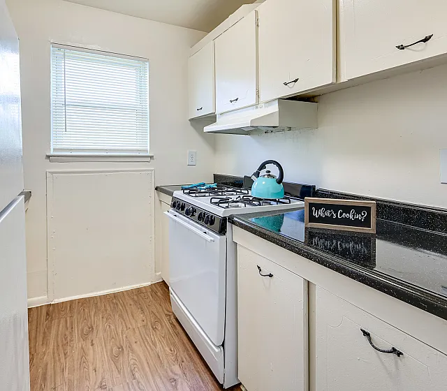 Charming kitchen boasting sleek black countertops, natural light, and efficient white cabinetry for a cozy culinary experience.