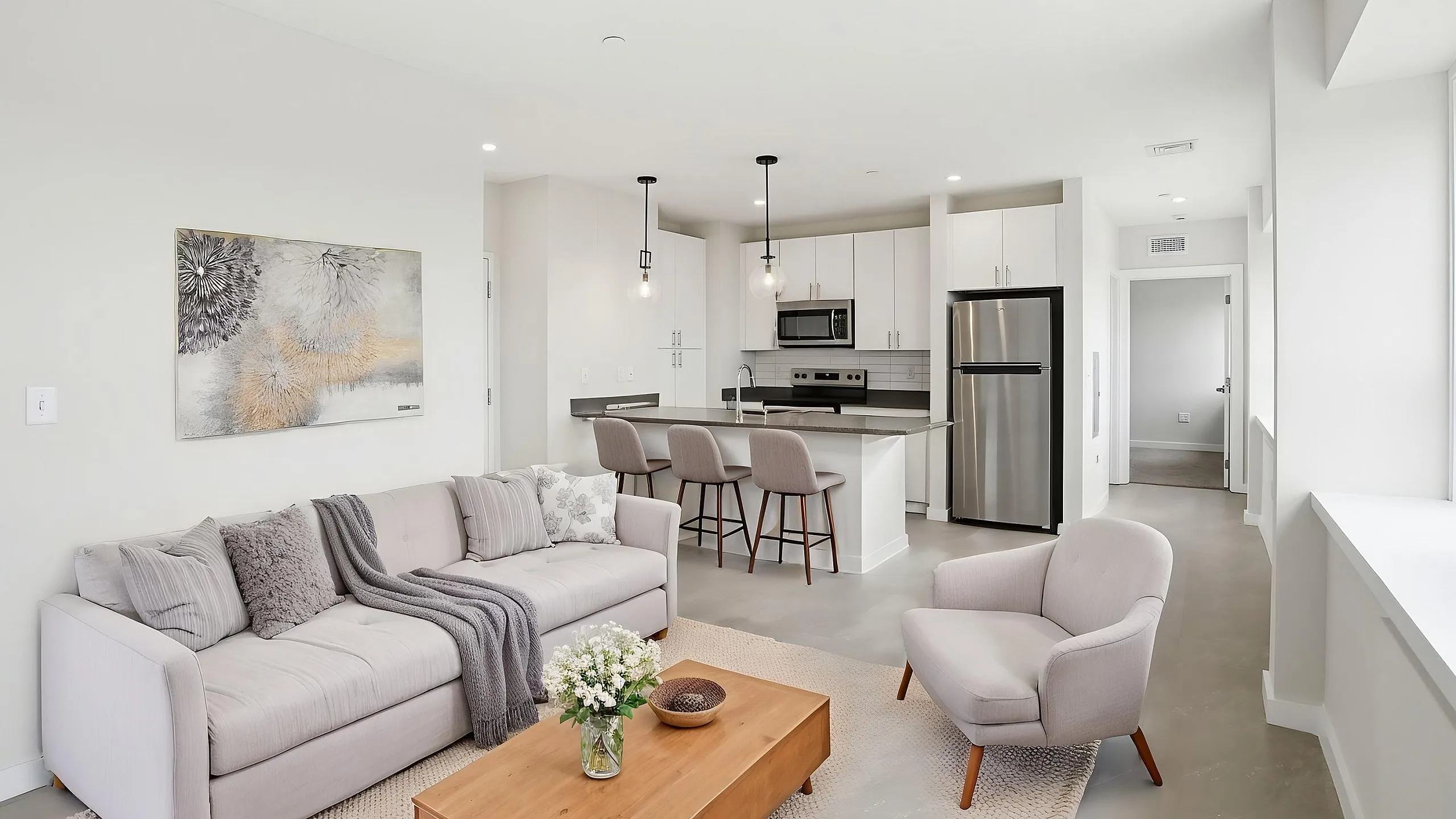Modern open-plan living area with cozy gray sofa, stylish armchair, and sleek kitchen featuring stainless steel appliances.