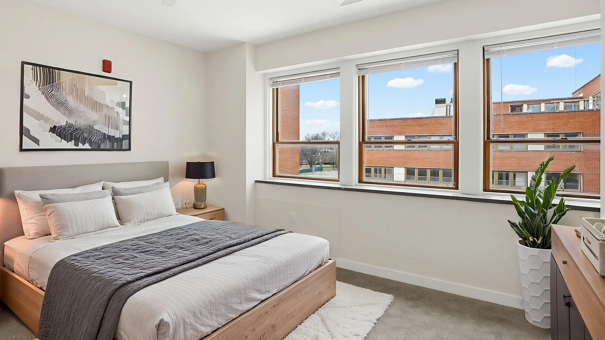 Bright and cozy bedroom featuring a stylish bed with plush pillows, modern ceiling fan, and large windows framing a scenic view.