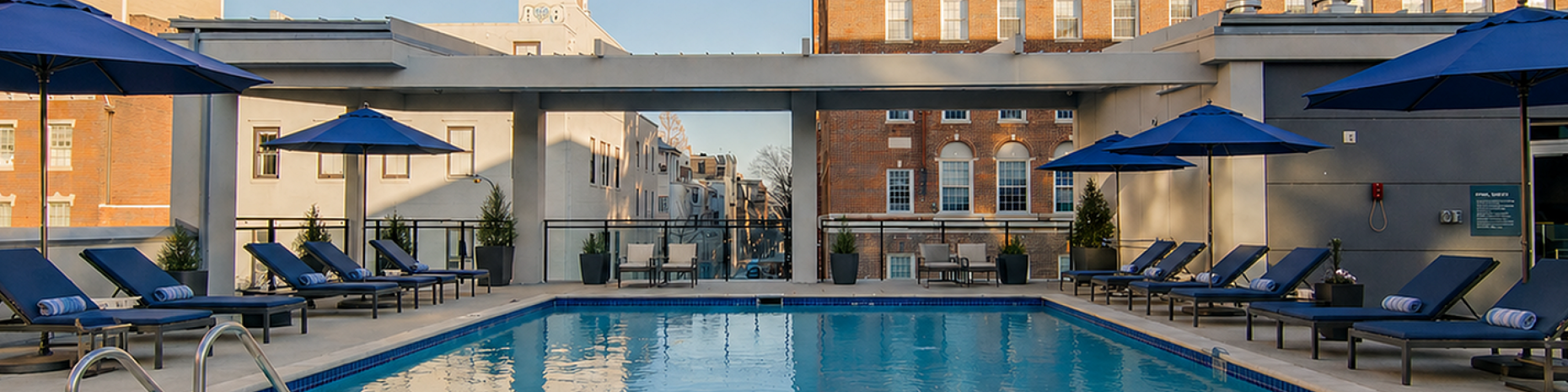 Elegant rooftop pool area with stylish loungers and blue umbrellas, perfect for relaxation and city skyline views.