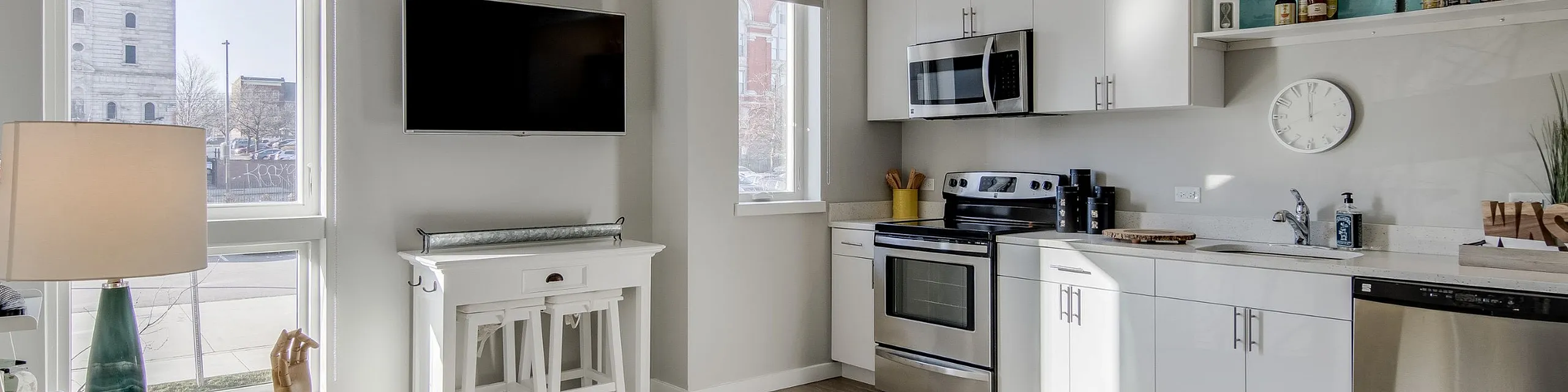 Bright and modern living space with sleek white kitchen, stainless steel appliances, and cozy yellow chair, offering a perfect blend of comfort and style.