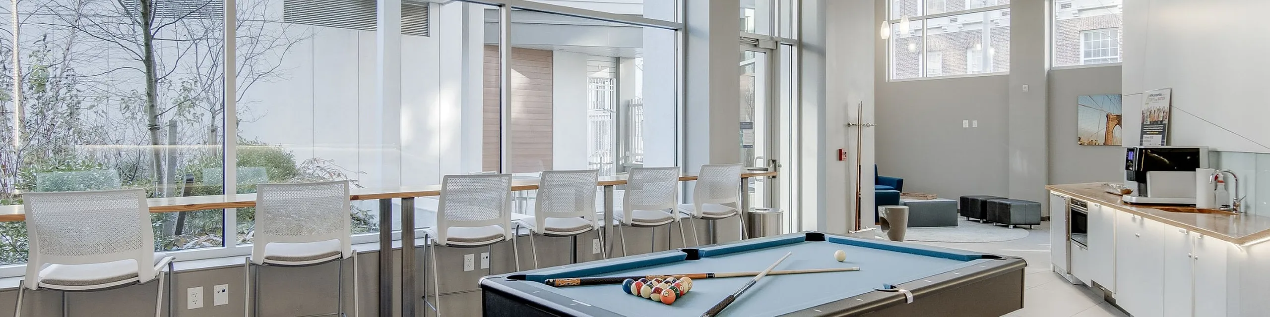 Modern communal space featuring a billiards table, ample seating, and large windows with natural light.