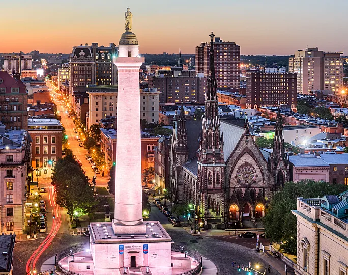 Majestic urban skyline with a prominent monument at sunset, surrounded by historic architecture and vibrant city lights.