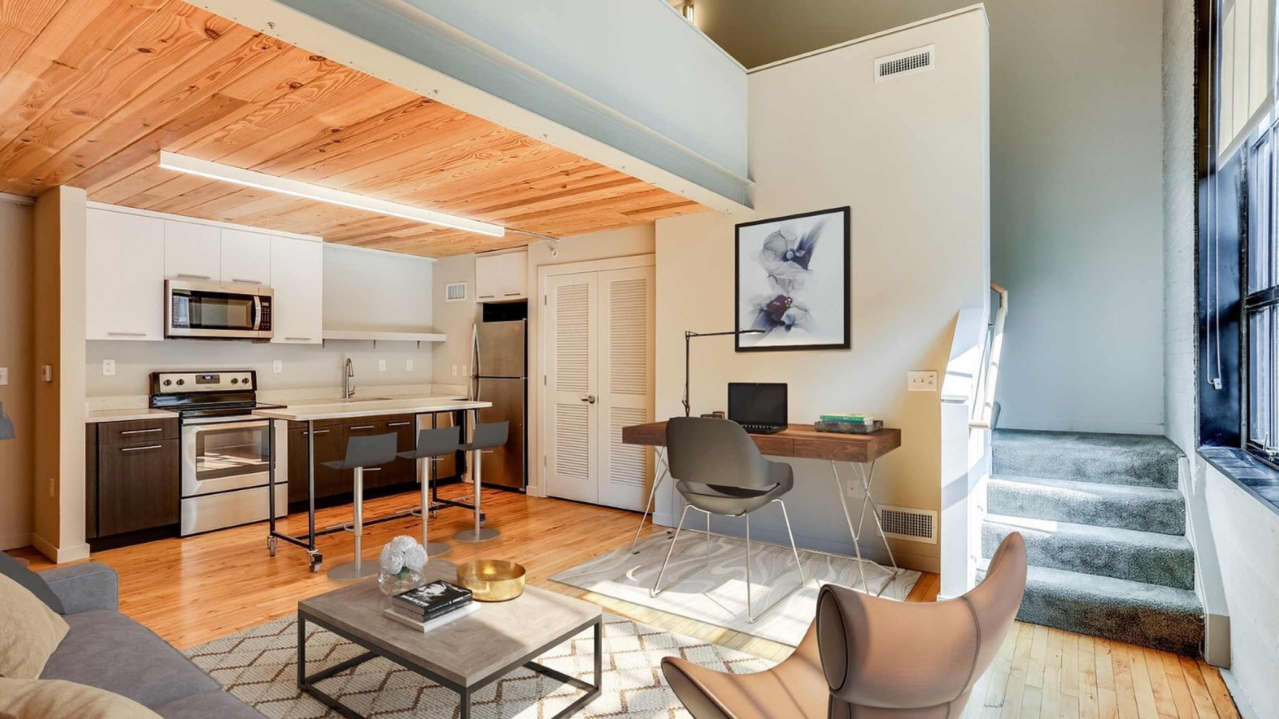 Chic loft-style apartment featuring an open-concept kitchen with modern appliances, cozy living area, and a bright workspace with large windows.