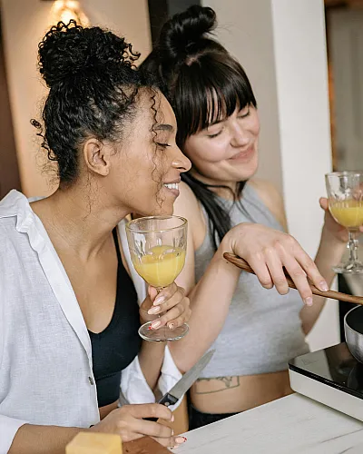 Two friends enjoying a joyful cooking session in a cozy kitchen, sipping orange juice and sharing smiles.