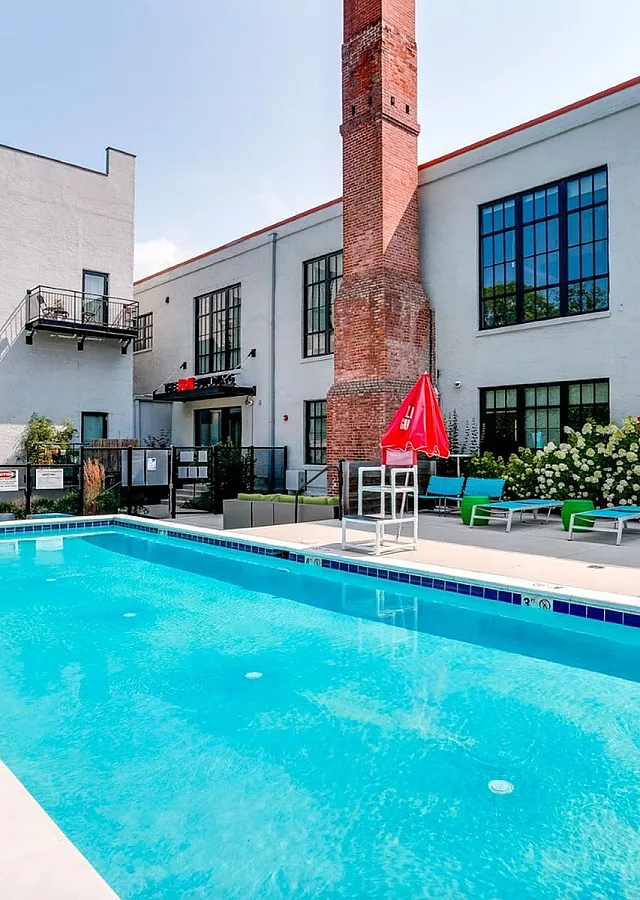 Charming apartment patio with a sparkling pool, vibrant outdoor seating, and lush greenery, perfect for relaxation and entertainment.