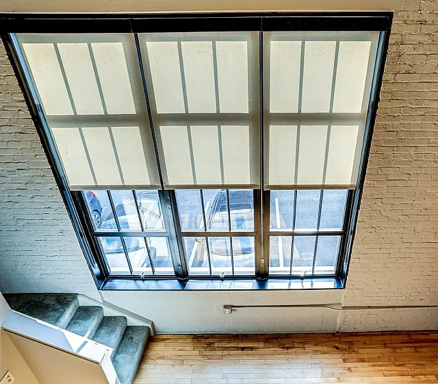 Chic loft apartment showcasing large industrial windows with elegant blinds, exposed brick walls, and a sleek wooden floor.