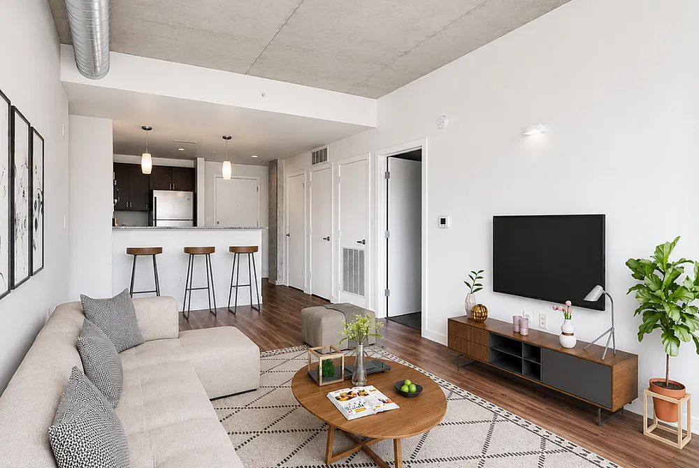 Modern open-concept apartment with stylish decor, featuring a cozy seating area, sleek kitchen with bar stools, and contemporary wooden flooring.